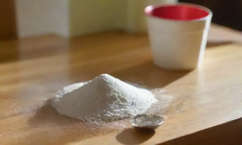 Una cocina iluminada con un mostrador desordenado, un bol de bicarbonato de sodio, lazos entre utensilios cotidianos y un gato curioso observando desde su cama