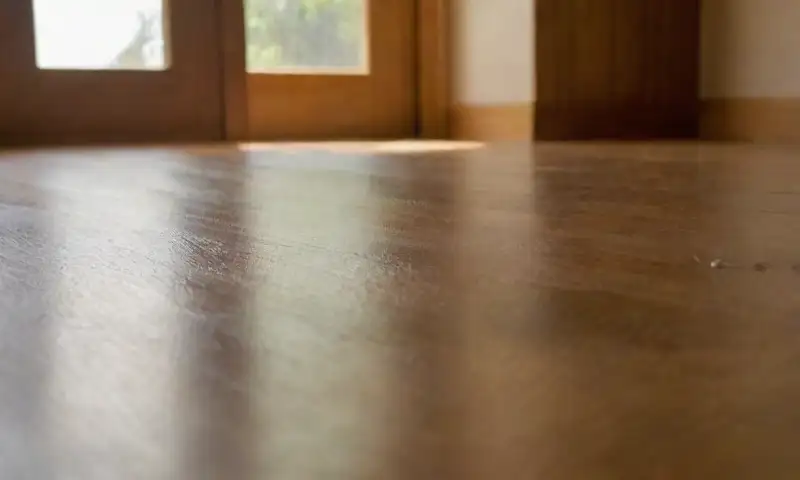 Un piso de madera bien iluminado con luz solar, personas limpiándolo, y un ambiente cálido y acogedor