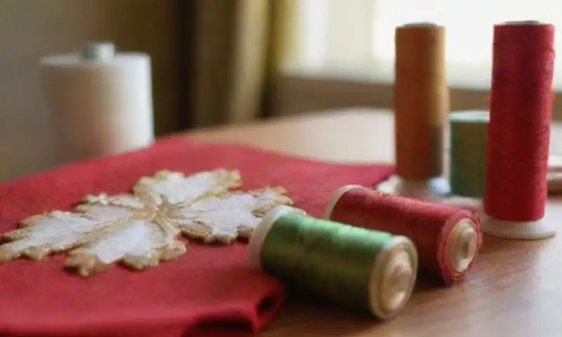 Una escena festiva de manualidades navideñas con tela de fieltro rojo, piezas de calcetín navideño, bordados de copos de nieve y una iluminación suave