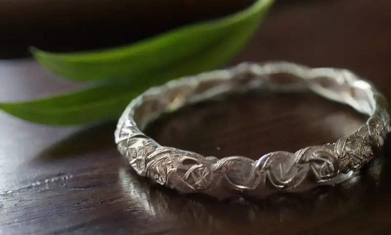 Un brazalete de plata vintage reposa sobre una mesa de madera oscura, acompañado de una bola de cerámica con pasta de dientes y un trapo para pulir, creando una atmósfera serena