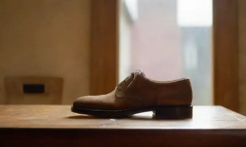 Zapatos de ante texturizados sobre una superficie de madera con herramientas de limpieza y un ambiente iluminado que invita a la información