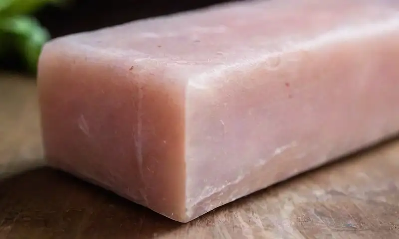 Un bloque pequeño de sal rosa del Himalaya brilla suavemente sobre una mesa de madera rústica, acompañado de romero fresco, evocando calma y pureza en un ambiente natural