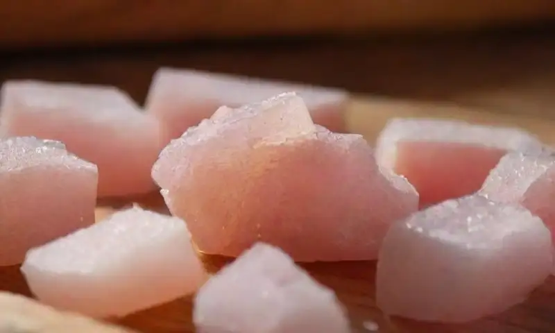 Cristales de sal luminosos en tonos rosa, blanco y naranja brillan sobre una superficie de madera rugosa, reflejando la luz y creando una atmósfera acogedora