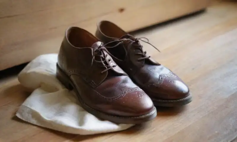 Unas viejas botas marrones con rasguños y los cordones desatados están sobre un suelo de madera