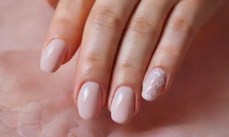 Uñas de almendra delicadamente pulidas y decoradas con arte de encaje blanco sobre un fondo cálido y herramientas de manicura desenfocadas