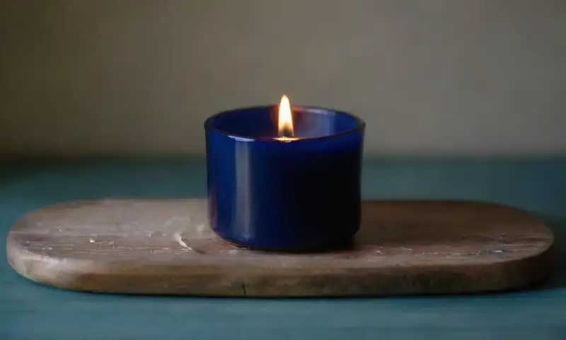 Una vela azul marina emite una suave luz cálida que resalta su textura y detalles, creando una atmósfera tranquila y vibrante