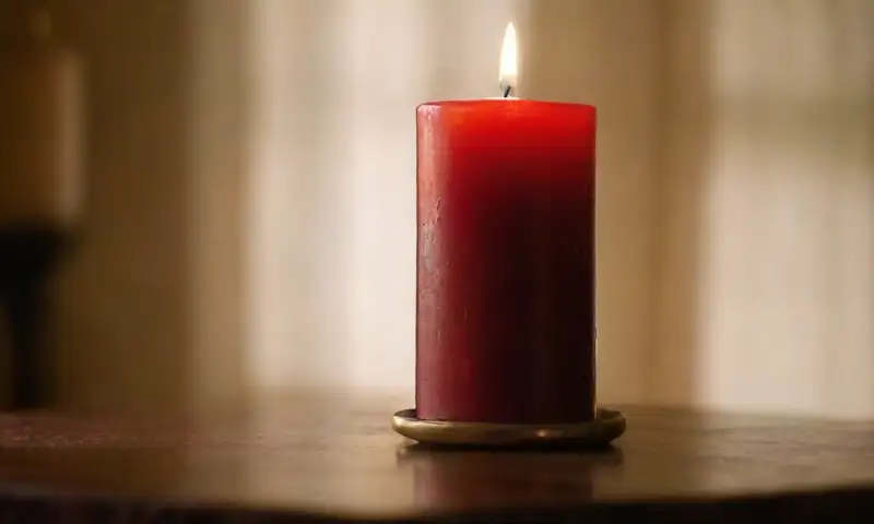 Una habitación tenue con una vela roja que ilumina suavemente, creando sombras y un ambiente sereno
